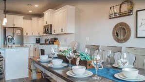 A modern kitchen with white cabinets, a central island with a blue placemat, and a dining area set for six with white plates and wine glasses. - Zion's Premier Getaway for the entire family!  (Hurricane)