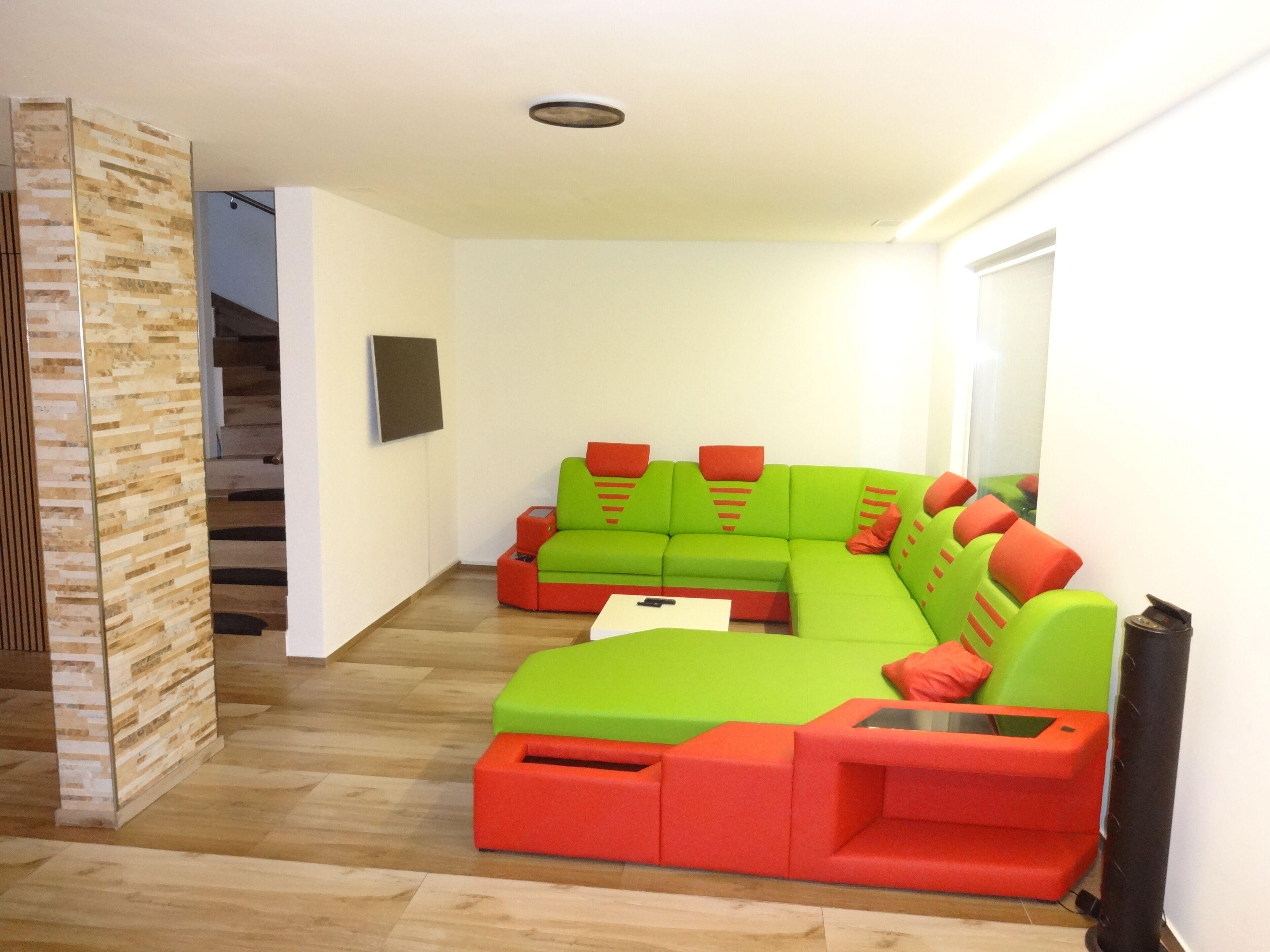 A modern living room with a green sectional sofa, red accent pillows, and a wooden floor.