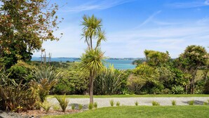 A landscaped garden with a variety of tropical plants and a view of the sea. - Tawharanui Cabin - Rural Cabin Studio (Warkworth)