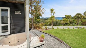 A house with a covered outdoor area, a small garden, and a view of the sea. - Tawharanui Cabin - Rural Cabin Studio (Warkworth)