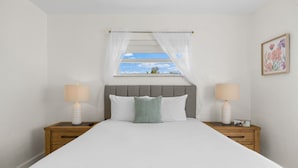 Une chambre à coucher avec un lit, deux tables de chevet avec des lampes, une fenêtre donnant sur un beau paysage et un tableau encadré au mur.