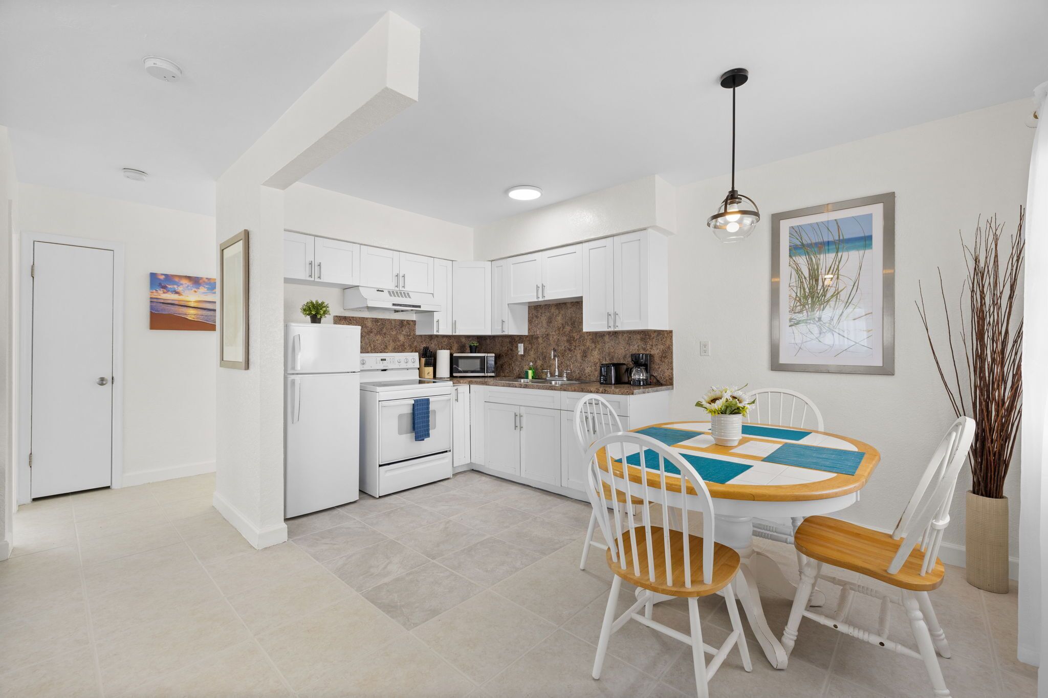 A modern kitchen with white cabinets, a dining table with chairs, and a hanging light fixture.