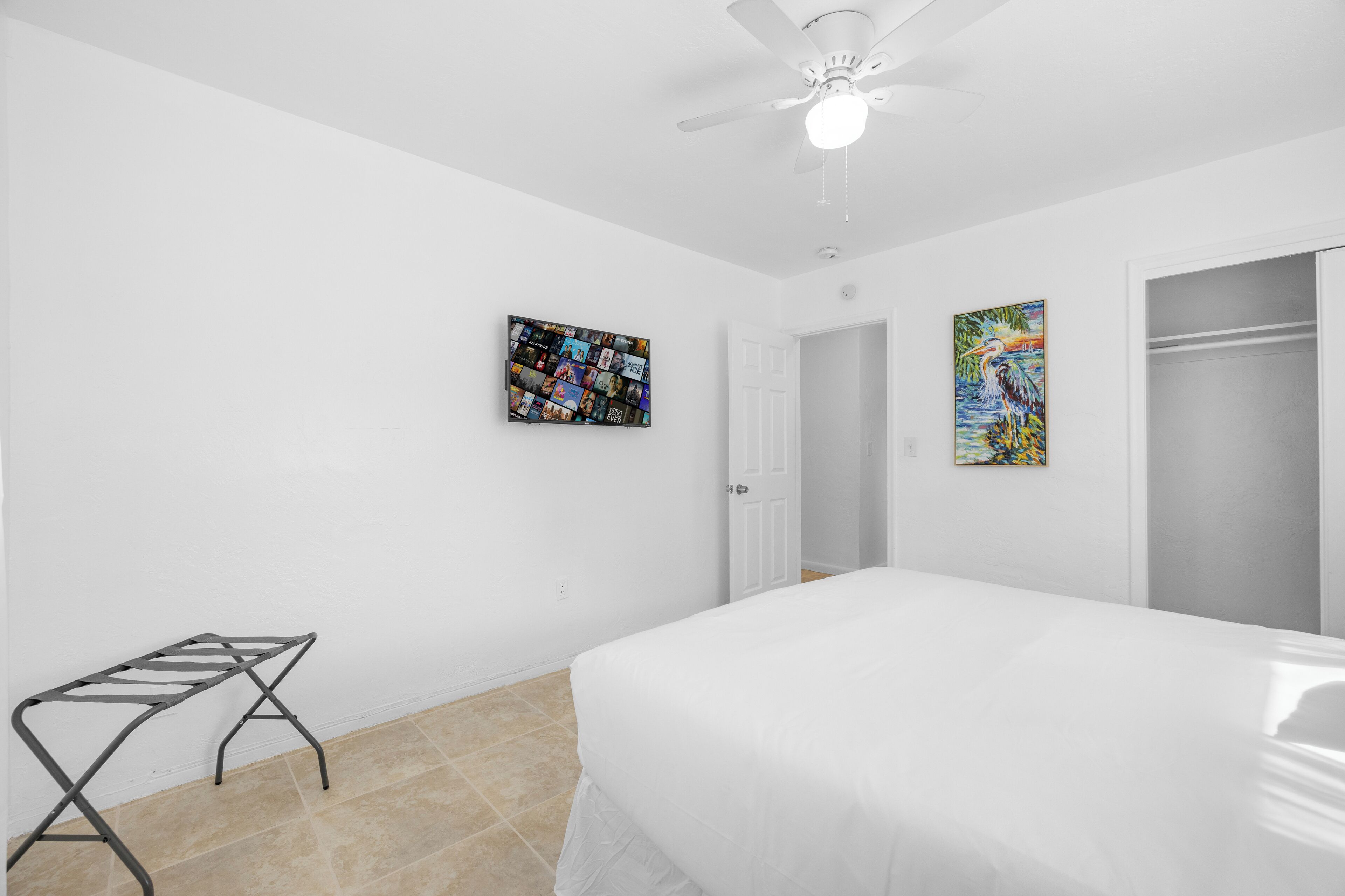 Une chambre à coucher avec un lit, un ventilateur de plafond, un téléviseur fixé au mur et deux tableaux.