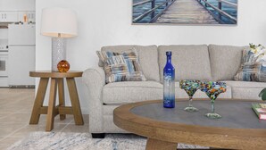 Un salon comprenant un canapé, une table basse, une lampe et un tableau représentant une jetée.