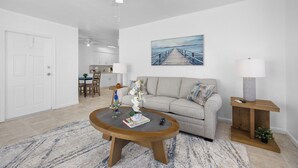 Un salon avec un canapé gris, une table basse en bois et un tableau représentant une jetée.