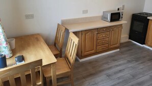A small kitchen with wooden cabinets, a microwave, and a stove. There is a dining table with chairs.