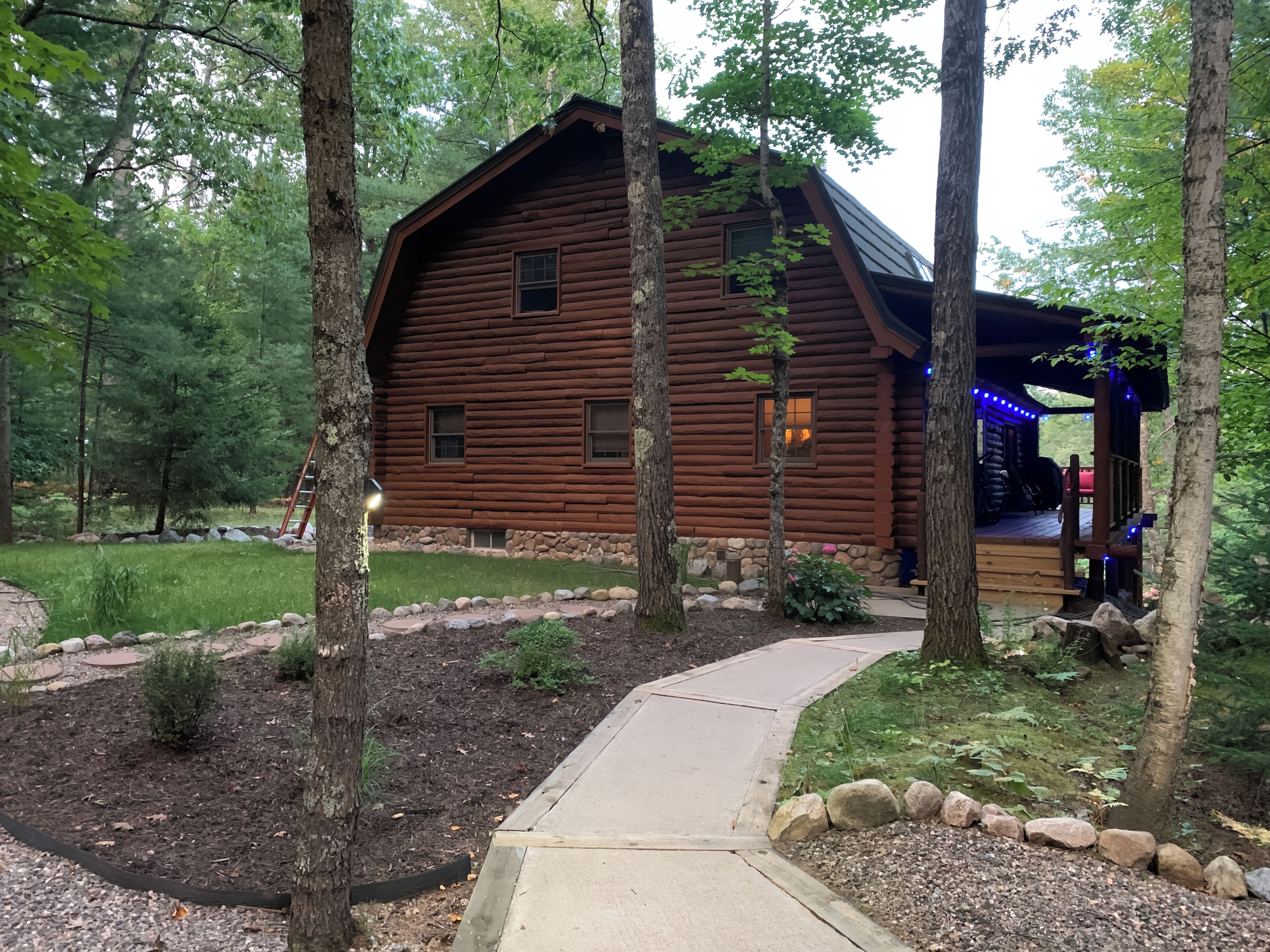 A log cabin with a porch, surrounded by trees and a stone pathway.