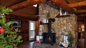 Un acogedor interior de cabaña de troncos con chimenea de piedra, vigas de madera y un árbol de Navidad.