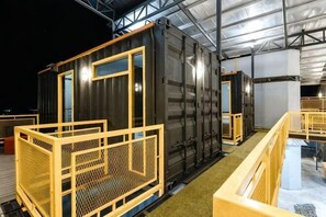 A large, dark-colored shipping container converted into a room with a wooden railing and a small window. - 7 Inn Semporna (Semporna)