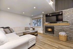 Ein modernes Wohnzimmer mit einem Ecksofa, einem Kamin, einem Flachbildfernseher und einem großen Fenster.