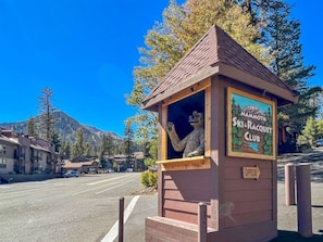 Une petite construction en bois, sur laquelle est apposée une enseigne indiquant le « Mammoth Ski & Racquet Club », située dans une rue bordée d’immeubles et d’arbres.