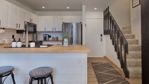 A modern kitchen with white cabinets, stainless steel appliances, a wooden island with stools, and a staircase with a dark railing. - Walkable to Canyon Lodge w/ Ski Locker (Mammoth Lakes)