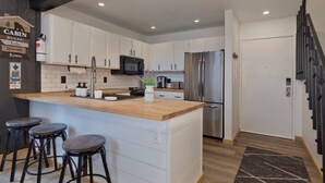 A modern kitchen with white cabinets, a stainless steel refrigerator, and a wooden island with bar stools. - Walkable to Canyon Lodge w/ Ski Locker (Mammoth Lakes)