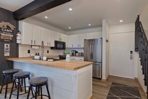 Eine moderne Küche mit weißen Schränken, einem Edelstahlkühlschrank und einer Holztheke mit Barhocker.