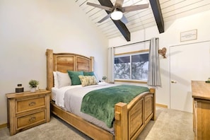 Ein Bett mit Holzkopfstütze, ein Nachttisch, ein Fenster mit Vorhängen und ein Deckenventilator.