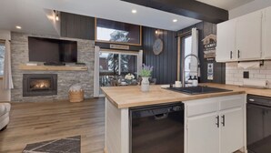 A modern kitchen with a stone fireplace, wooden countertops, and white cabinetry. - Walkable to Canyon Lodge w/ Ski Locker (Mammoth Lakes)