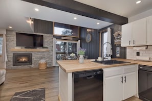 Une cuisine moderne avec une cheminée en pierre, des plans de travail en bois et des meubles de cuisine blancs.