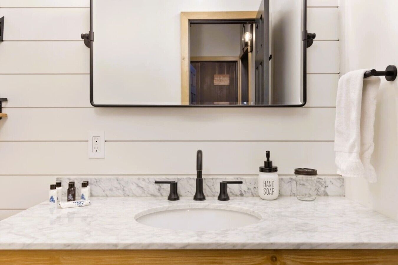 A bathroom with a white marble sink, black faucet, and a hand soap dispenser.