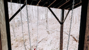 A hammock swing under a wooden pergola with stone flooring and a view of a snowy landscape.