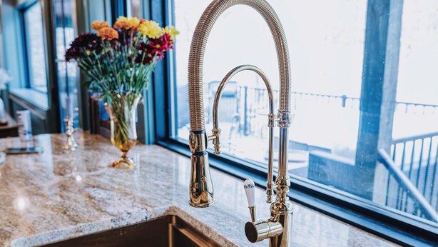 A kitchen with a stainless steel sink, a vase with flowers, and a window with a view of a bridge.