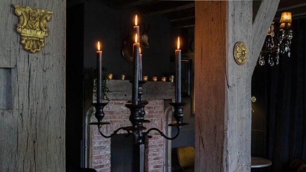Un interior rústico con chimenea de ladrillo, un candelabro con velas encendidas y una araña.