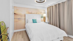 A bedroom with a bed, a headboard, a nightstand with a lamp, a wall with a painting, and a window with curtains. - Amazing Ocean Front Property on Daytona Beach with amazing views & full kitchen (Daytona Beach)