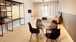 Une pièce moderne et bien éclairée, comprenant une table et des chaises, un canapé, un lit et une armoire intégrée avec des étagères et des porte-manteaux.