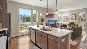 Une cuisine moderne dotée d’un îlot central, de grandes fenêtres et d’un coin repas avec un canapé et une table.