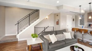 Un salon moderne avec un canapé gris, une petite table blanche et un escalier.