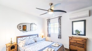 Een slaapkamer met een bed, een houten dressoir, een spiegel en een plafondventilator.