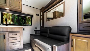 A compact RV interior with a kitchenette, a sofa bed, and a large window with a forest view. - The Happy Camper - Cozy RV sleeps 4, with WiFi, in beautiful Ojai (Ojai)