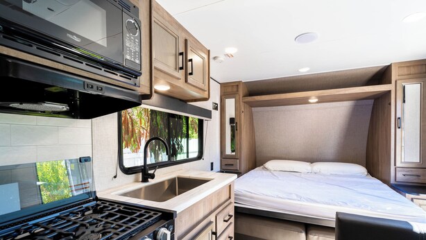 A compact RV interior with a kitchenette, a bed, and a small bathroom. - The Happy Camper - Cozy RV sleeps 4, with WiFi, in beautiful Ojai (Ojai)
