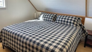 A bedroom with a checkered bedspread, a wooden headboard, and a window with blinds. - Big Bend Lodging at Ten Bits Ranch - Room #15 -  Freight Office (Terlingua)