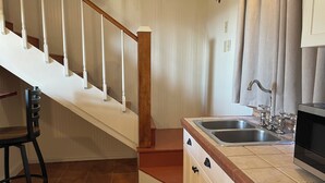 A kitchen with a wooden staircase, a black chair, a double sink, and a microwave. - Big Bend Lodging at Ten Bits Ranch - Room #15 -  Freight Office (Terlingua)
