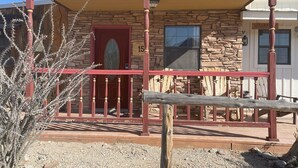 A rustic stone building with a red door and a porch. - Big Bend Lodging at Ten Bits Ranch - Room #15 -  Freight Office (Terlingua)