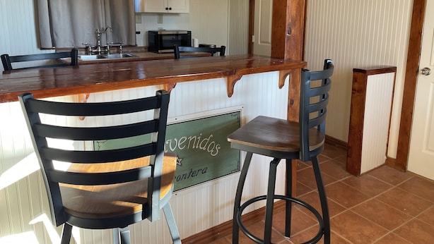 A kitchen with a wooden bar counter, two chairs, a sign reading "Caminito," and white cabinets. - Big Bend Lodging at Ten Bits Ranch - Room #15 -  Freight Office (Terlingua)
