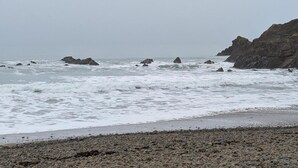Una playa rocosa con olas rompiendo en la orilla y grandes rocas en el agua.