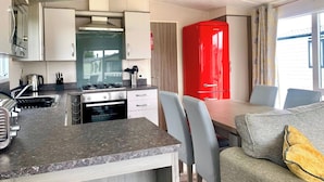 Una cocina compacta con estufa, lavamanos y armarios, un comedor con mesa y sillas, y un electrodoméstico rojo al fondo.