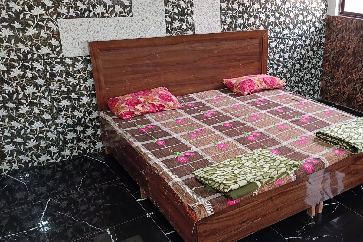 A bed with a floral-patterned bedspread and two pillows, a wooden headboard, and a marble-patterned wall behind it.