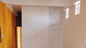 Ένα ευρύχωρο δωμάτιο με πλακάκι στο δάπεδο, έναν ανεμιστήρα οροφής και έναν τοίχο από τούβλα.