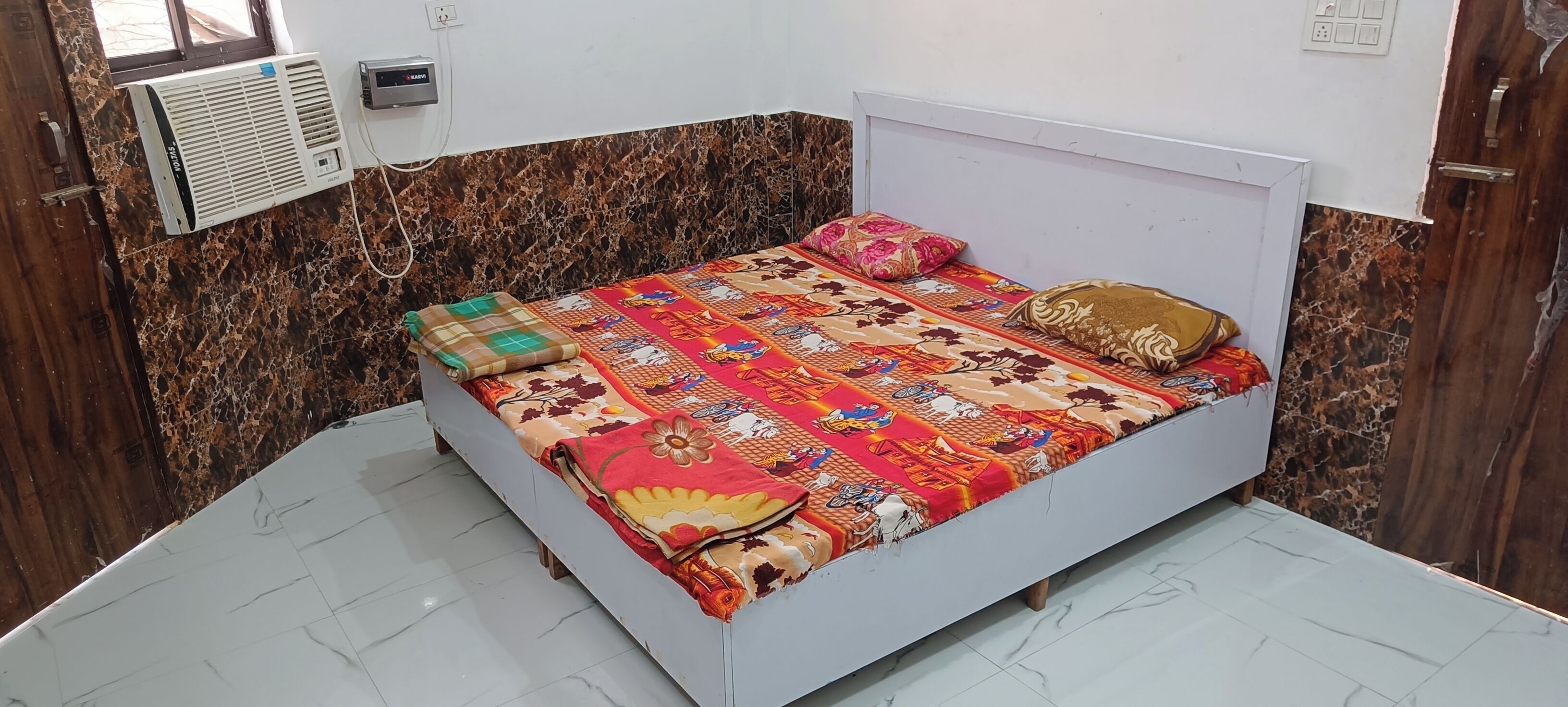A bedroom with a bed, a wall-mounted air conditioner, and a marble-patterned wall.