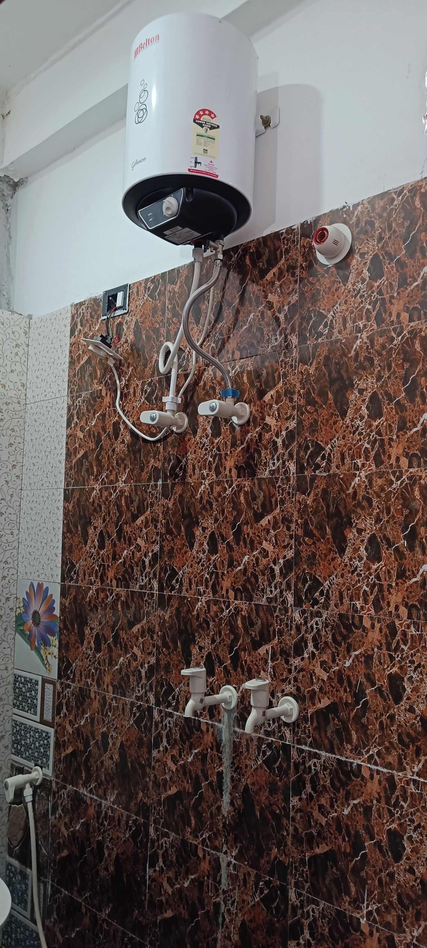 A bathroom with a marble wall, a ceiling-mounted heater, and a showerhead.