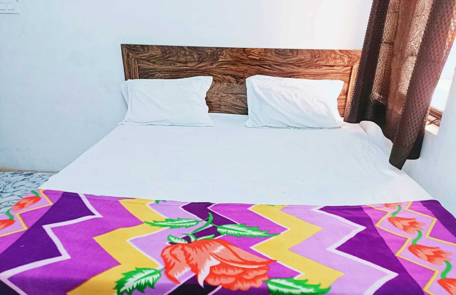 Uma cama com cabeceira de madeira, roupa de cama branca e um cobertor colorido estampado com flores.