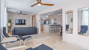 A spacious living area with a sofa, lounge chairs, ceiling fans, a kitchen in the background, and a large mirror on the wall. - Cozy Retreat in San Juan

 (san juan)