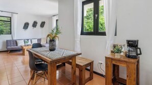 Una habitación acogedora con una mesa de madera, sillas, un pequeño centro y un sofá, además de una ventana con cortinas.