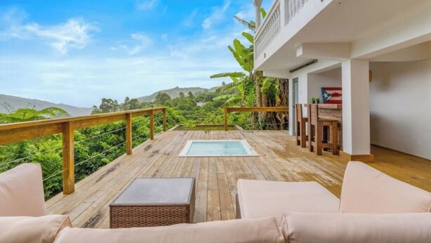 Una terraza de madera con un jacuzzi, asientos exteriores y vistas a las colinas.
