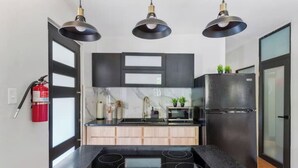 Una cocina moderna con encimeras negras, estufa negra, refrigerador negro y tres lámparas colgantes.