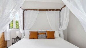 Un dormitorio con cama a dosel, ropa de cama blanca y dos almohadas.