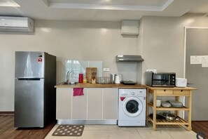 Eine kleine Küche mit Kühlschrank, Waschmaschine, Mikrowelle und Holztisch.