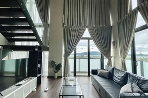 Ein modernes Wohnzimmer mit Sofa, Couchtisch und Fernseher. Eine Treppe befindet sich links, und ein Balkon bietet einen Blick ins Freie.